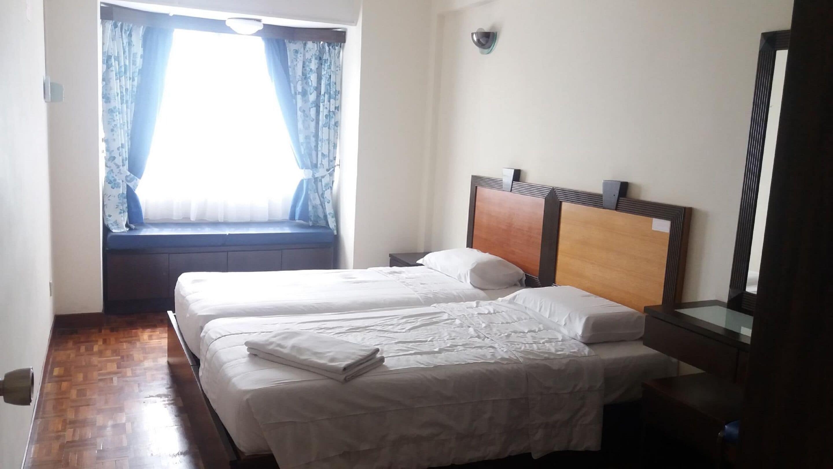Una habitación de hotel con dos camas, una ventana con cortinas, un cabecero de madera y un espejo.