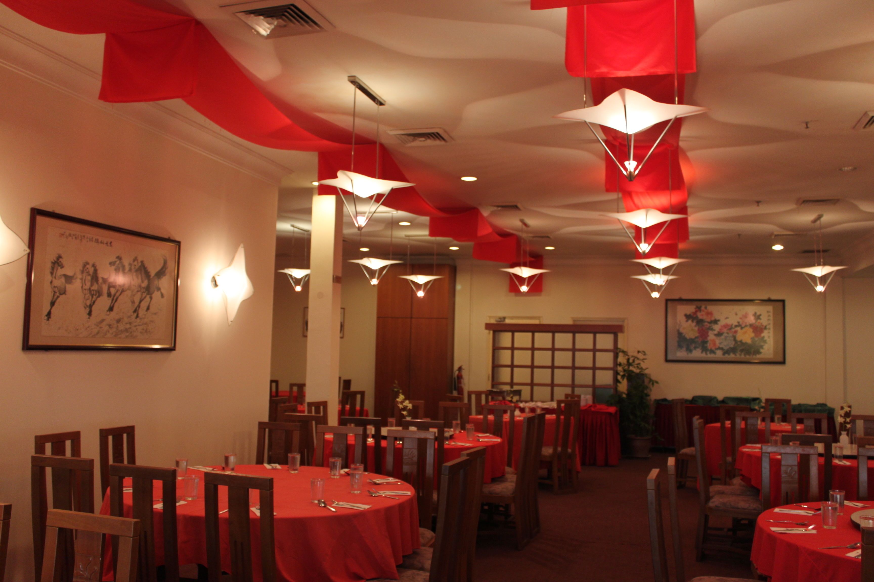 A dining area with round tables covered in red tablecloths, wooden chairs, and hanging pendant lights.