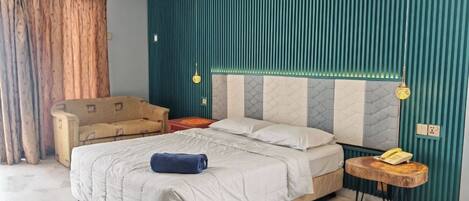 A bedroom with a bed, a sofa, a bedside table with a phone, and a wall with vertical lines.