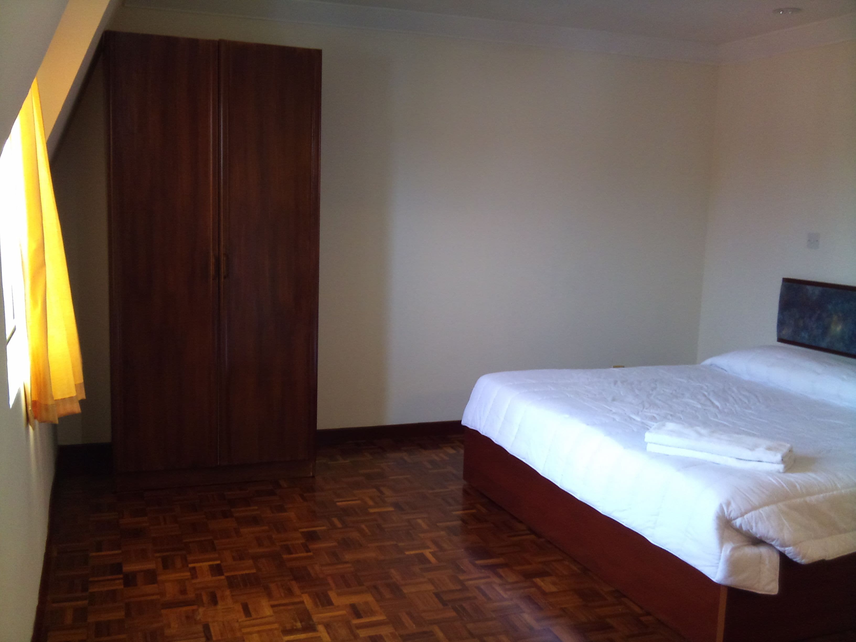 Un dormitorio con un armario de madera, una cama con ropa de cama blanca y un suelo de parqué de madera.