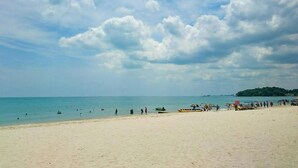 A beach with people and boats, a clear sky, and a distant island. - Bayu Beach Resort (Port Dickson)