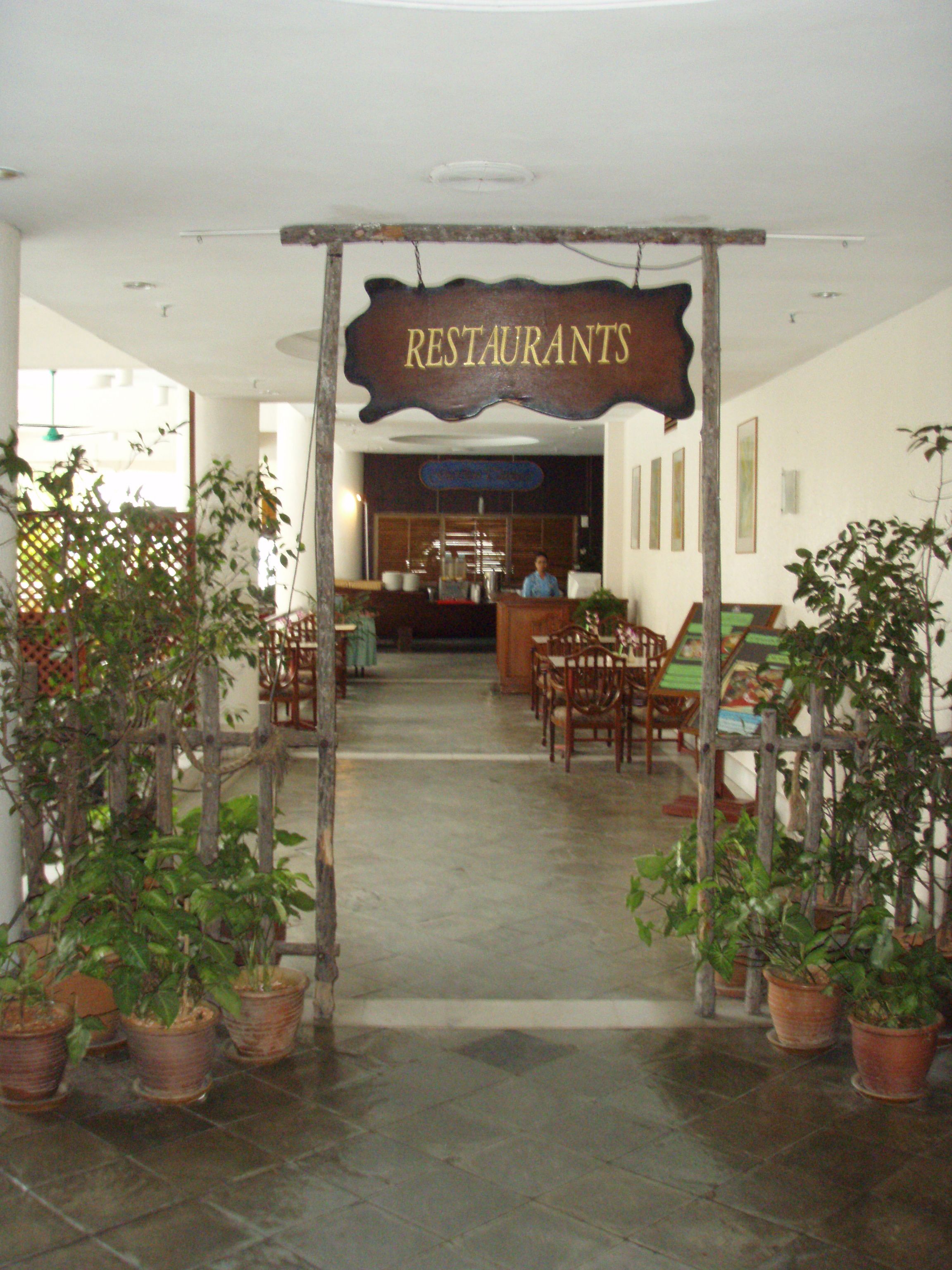 A restaurant entrance with a sign, potted plants, and a reception desk.