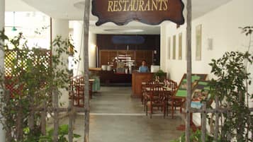 A restaurant entrance with a sign, potted plants, and a reception desk.