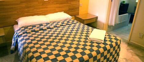 A hotel room with a checkered bedspread, wooden headboard, bedside tables, and a view of the bathroom.