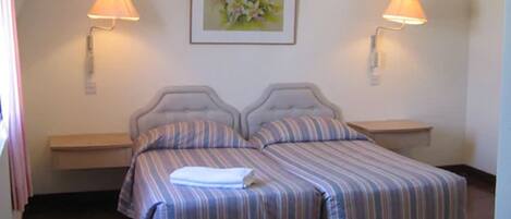 A double bed with striped bedding, two bedside lamps, a framed floral artwork on the wall, and a wooden floor.