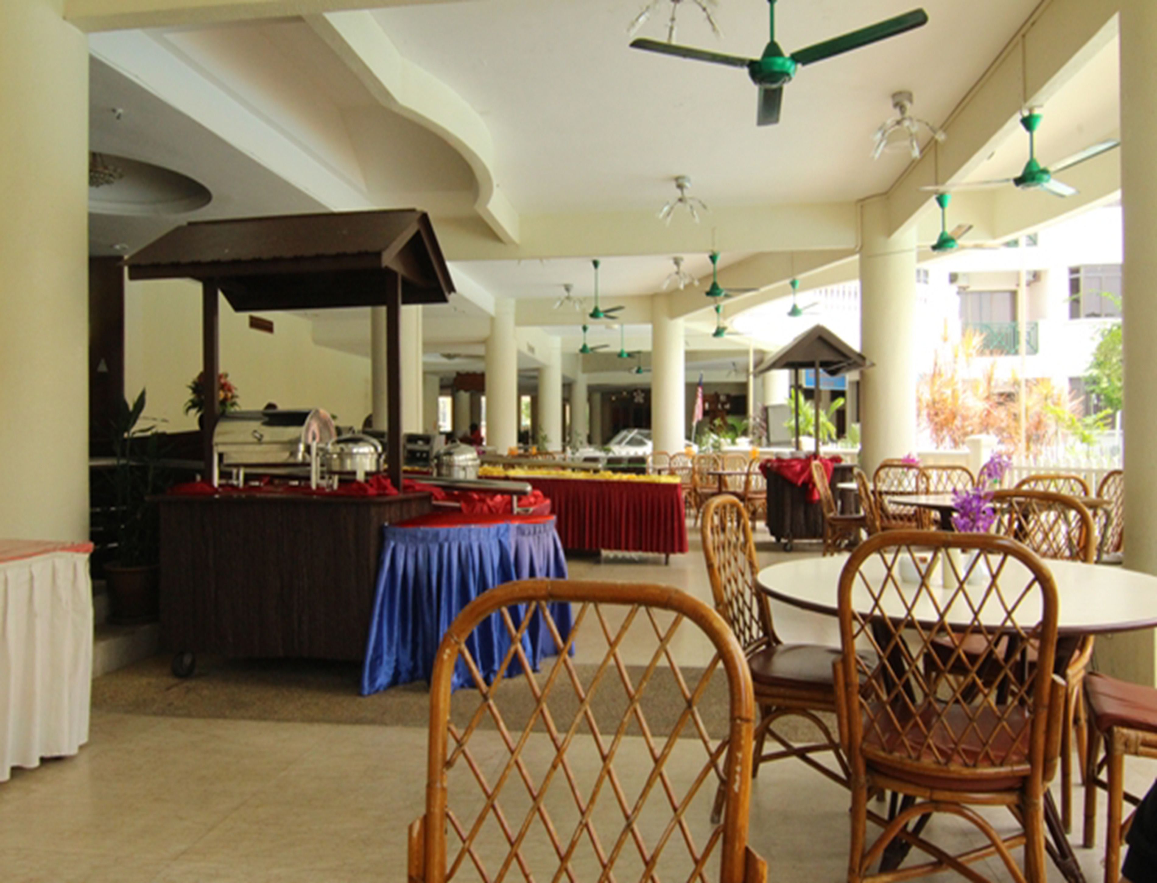 Un amplio espacio al aire libre con comedor, sillas y mesas de mimbre, ventiladores de techo y una mesa de buffet.