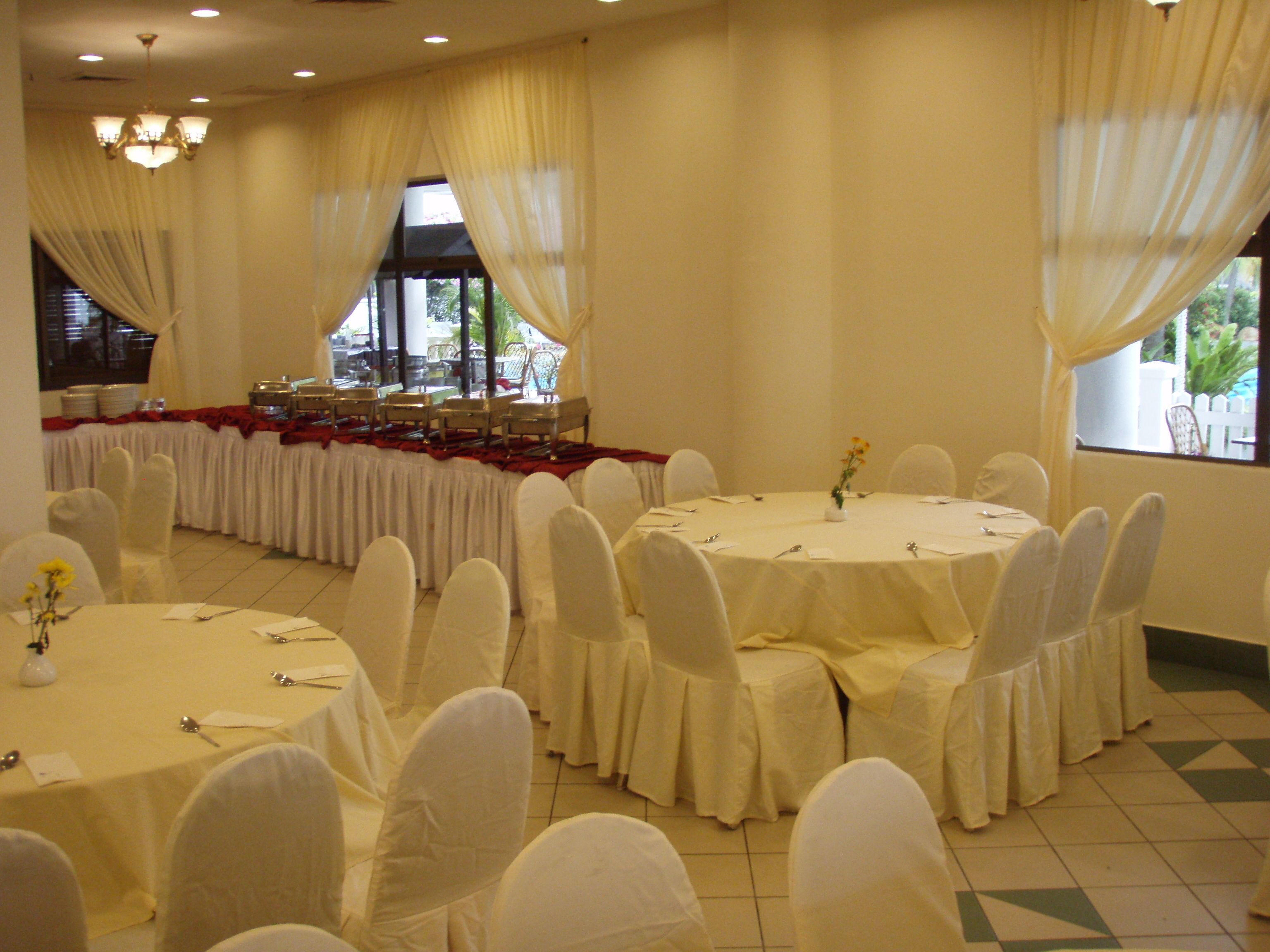 A banquet hall with round tables, white chairs, and a long table with chairs set up for a meal.