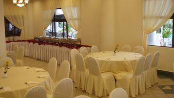 A banquet hall with round tables, white chairs, and a long table with chairs set up for a meal.