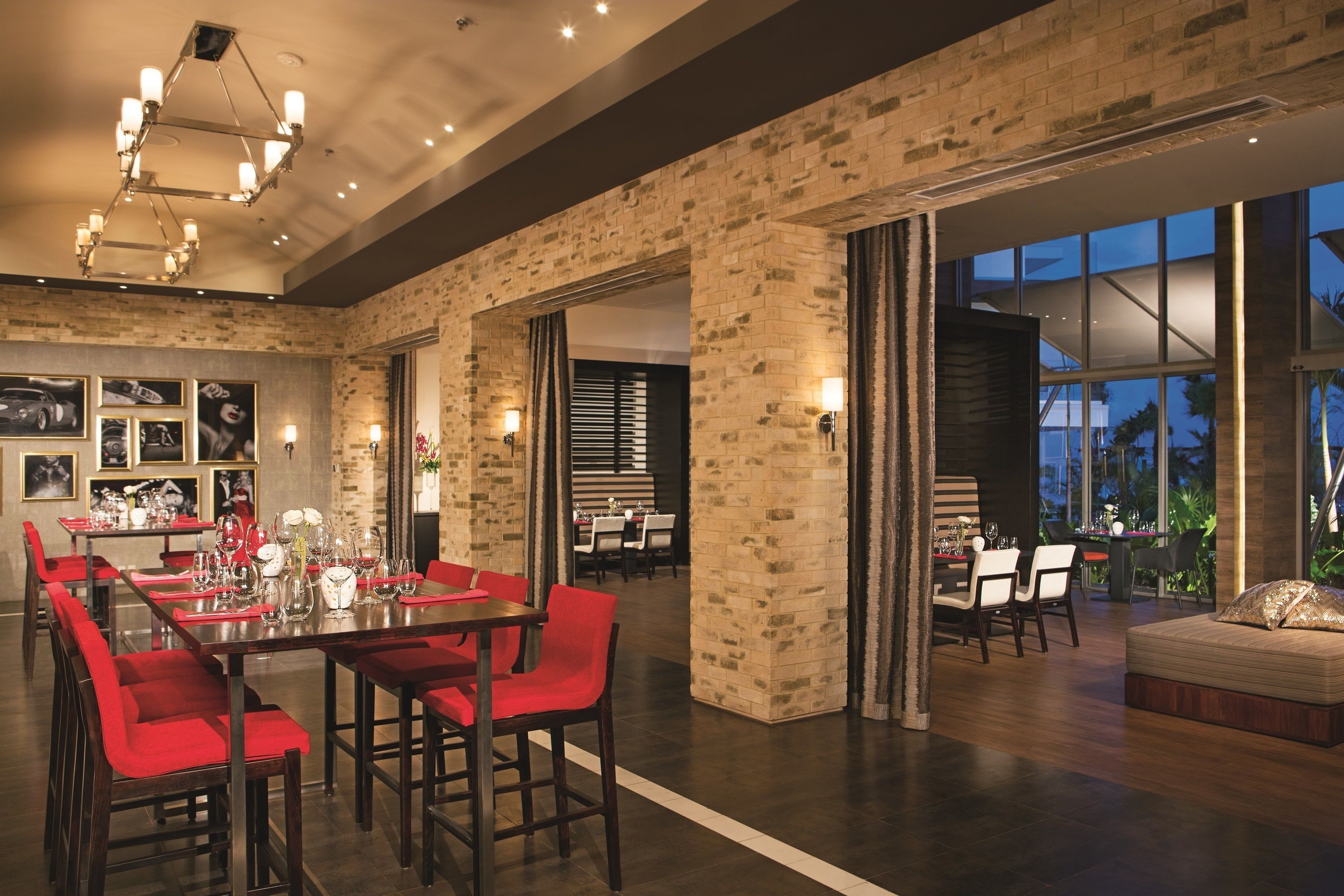 A spacious dining area with red chairs and a long table, brick walls, and large windows offering a view of the outdoors.