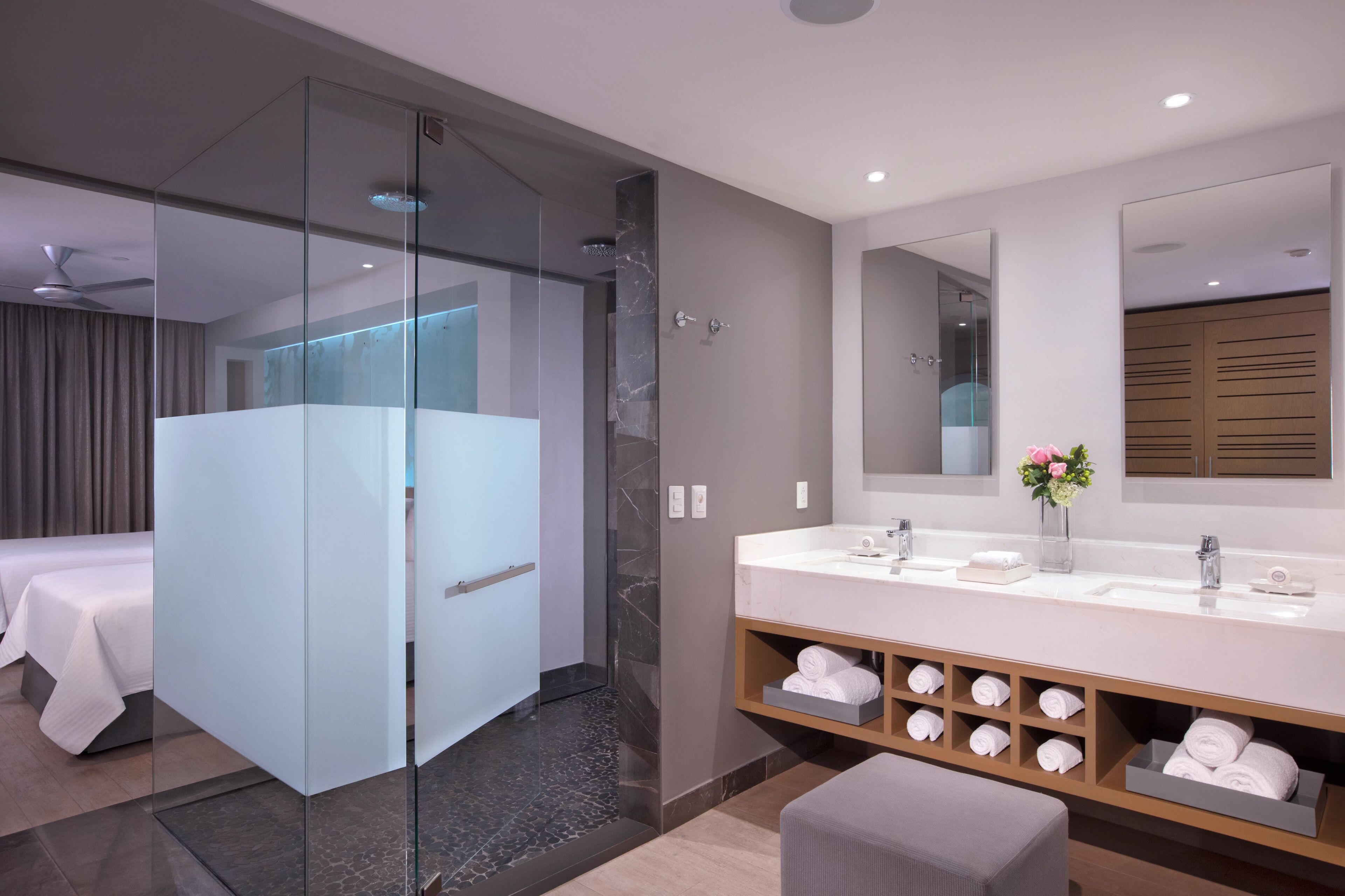 Une salle de bain d’hôtel moderne, dotée d’une douche à parois de verre, d’un grand meuble-lavabo avec miroir et de serviettes soigneusement rangées.