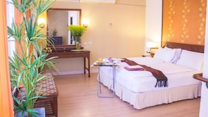 Habitación de hotel con cama, mesita de noche, un escritorio con silla, planta en maceta y espejo.