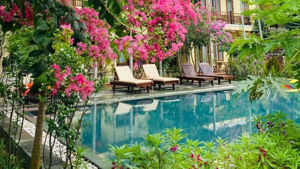 Área de piscina com espreguiçadeiras e um edifício com varandas.