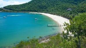 Uma praia com águas turquesa cristalinas, areal arenoso e uma colina arborizada ao fundo.
