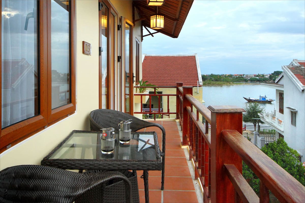 A balcony with wicker furniture, a glass table, and a view of a river and buildings.