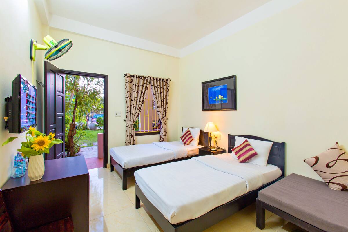 A hotel room with two beds, a desk with a vase of sunflowers, a TV, and a window with curtains.