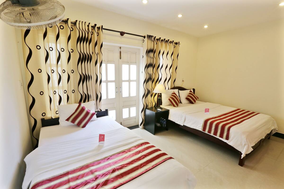 A hotel room with two beds, a nightstand, a lamp, and curtains with a wavy pattern.