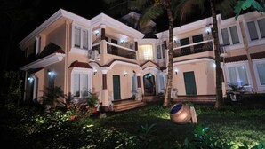 Una casa de dos pisos con un balcón, un porche delantero y un jardín iluminado durante la noche.