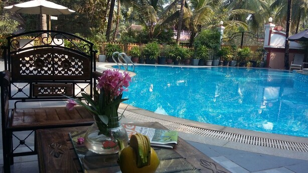 Una zona de piscina con un banco de madera, una mesa con un jarrón de flores y un periódico.