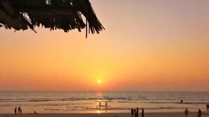 Una playa con un atardecer, gente caminando y sombrillas de playa.