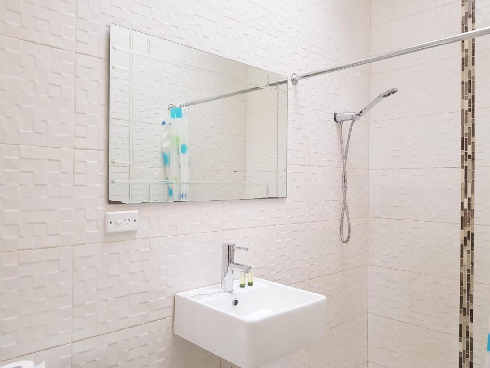Een badkamer met een wit wastafel, een spiegel en een douche.