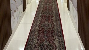 A long, narrow hallway with a patterned carpet, white tiled floor, and wooden paneling on the walls. - Perth City Motel (Thornlie)