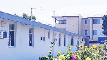 A row of white buildings with multiple windows, a paved walkway, and some greenery in the foreground.