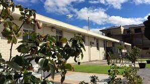 A building with a flat roof, a visible antenna, and a paved area with potted plants. - Perth City Motel (Thornlie)