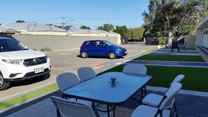 A residential street with two parked cars, a patio table with chairs, and a well-maintained lawn. - Perth City Motel (Thornlie)
