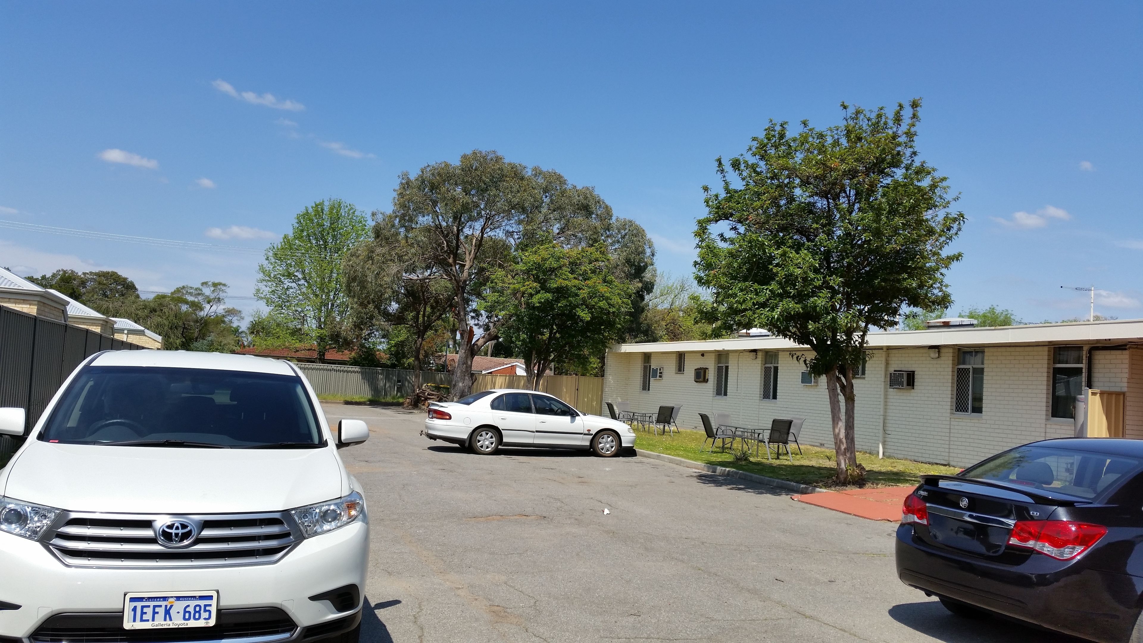 A residential street with parked cars, houses, and trees.