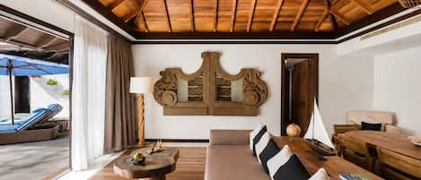 Een ruime woonkamer met een hoge nok, een grote bank, een houten salontafel en een eettafel met stoelen.