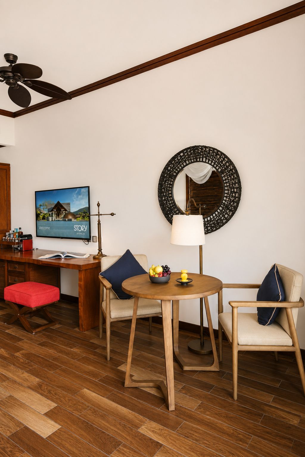 A room with a wooden desk, a television, a round table with chairs, a lamp, and a decorative mirror.