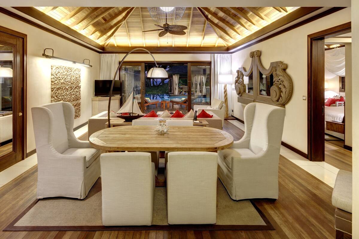 A spacious dining area with a round wooden table, white upholstered chairs, and a ceiling fan.