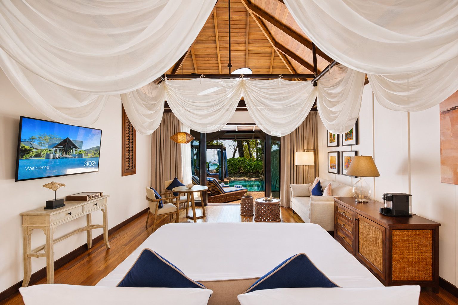 Habitación de hotel con cama, televisión, escritorio, silla, sofá, lámpara y vista a una piscina al aire libre.