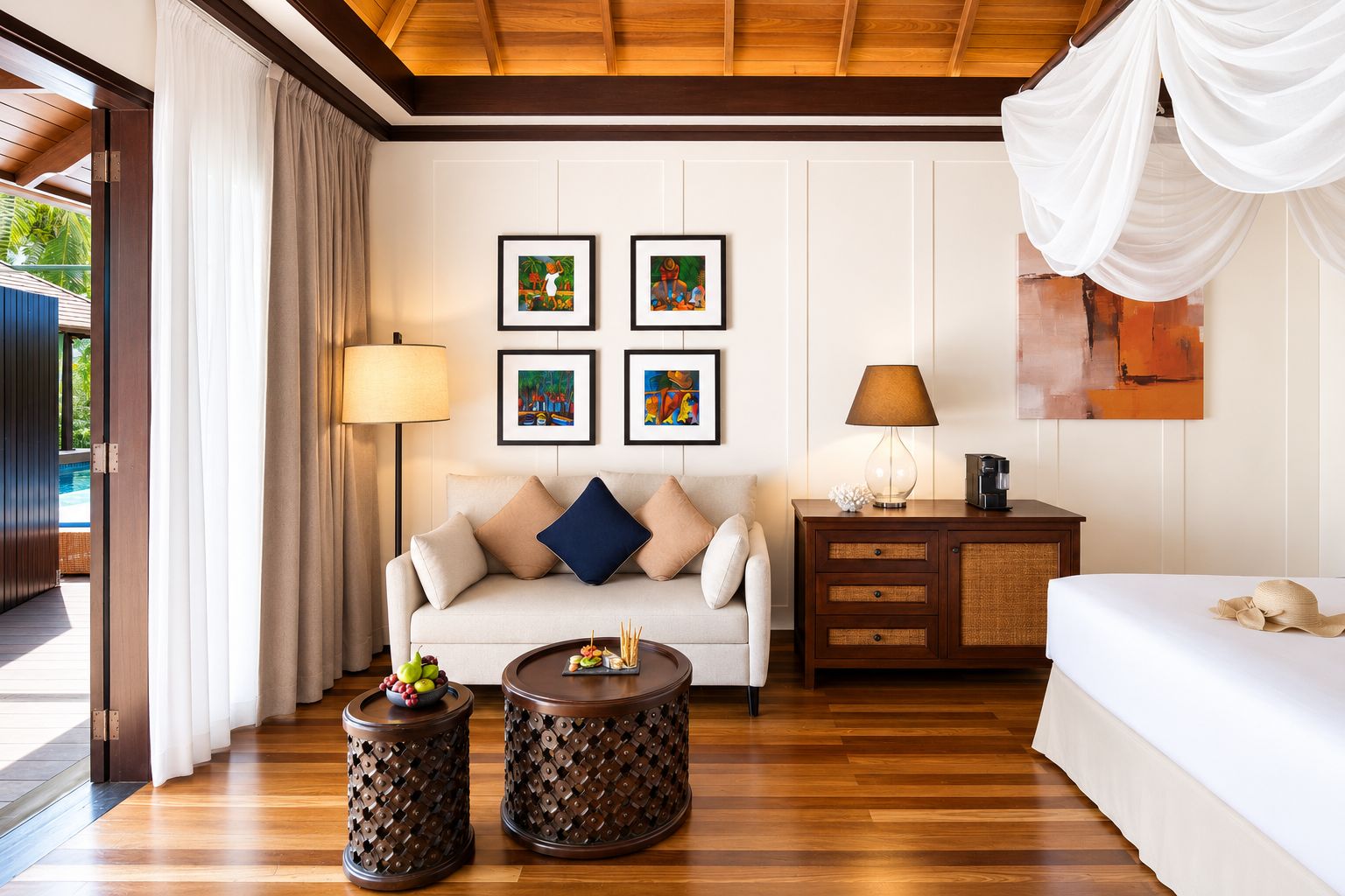 Een hotelkamer met een houten vloer, een bank, een bed, een nachtkastje, een lamp, een fotolijstje en uitzicht op een zwembad.