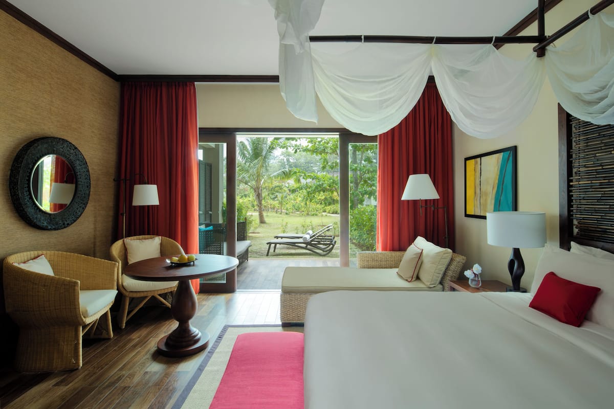 A hotel room with a bed, two chairs, a small table, a lamp, and a view of the outdoors.