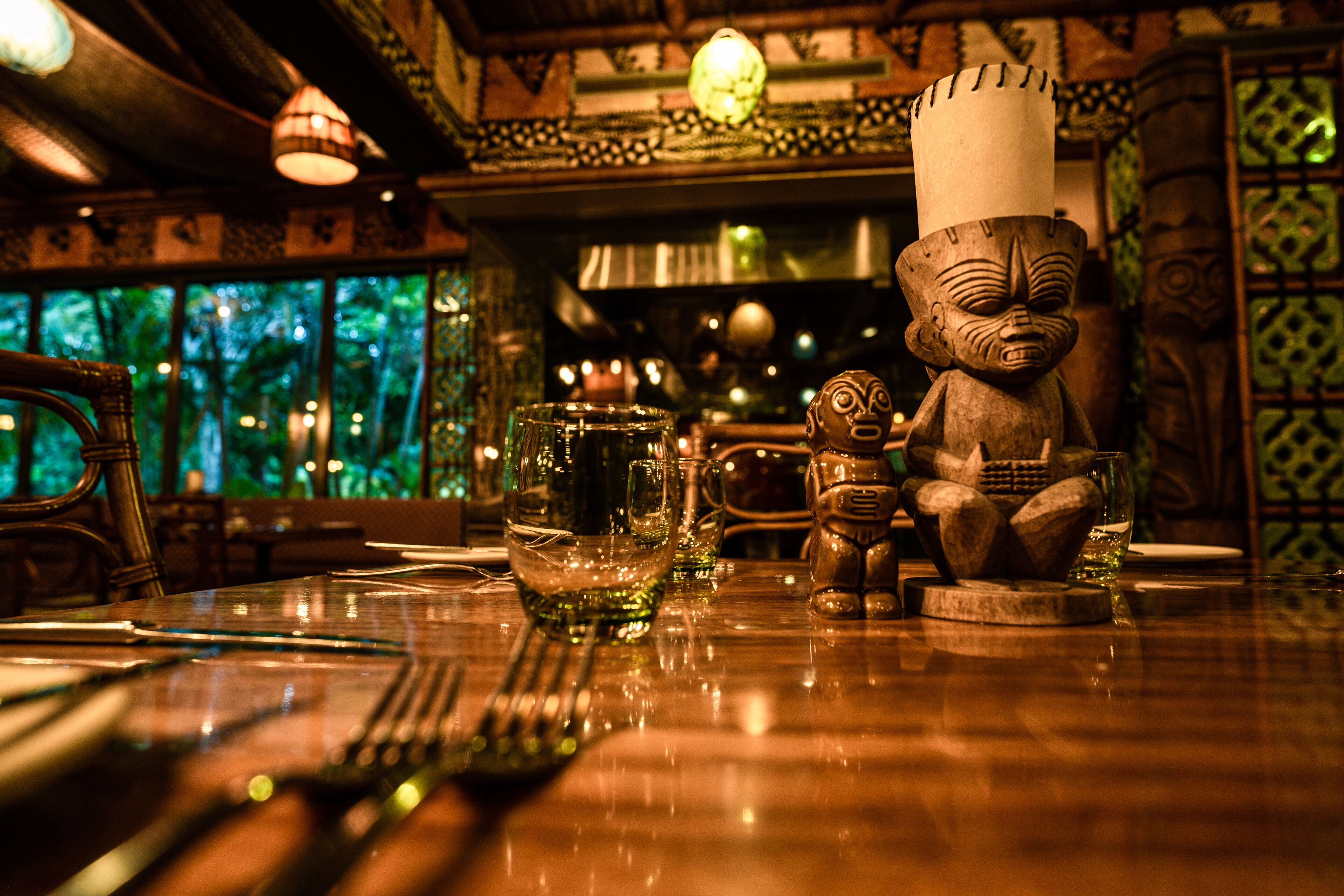A dining table with a wooden statue, a glass, and a candle.