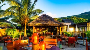 A beachside restaurant with outdoor seating, palm trees, and a thatched-roof structure. - STORY Seychelles (Mahé Island)