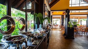 A buffet area with various food stations, a seating area with tables and chairs, and a view of greenery outside.