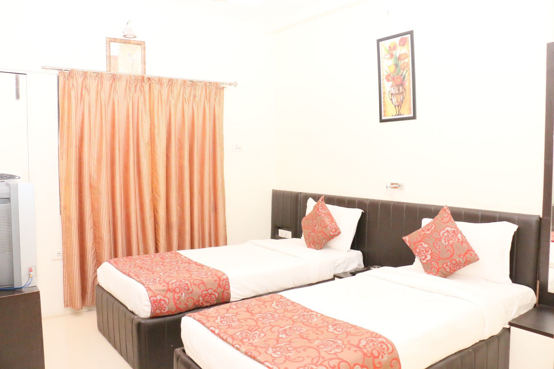 A hotel room with two beds, a TV, a curtain, and a framed picture on the wall.
