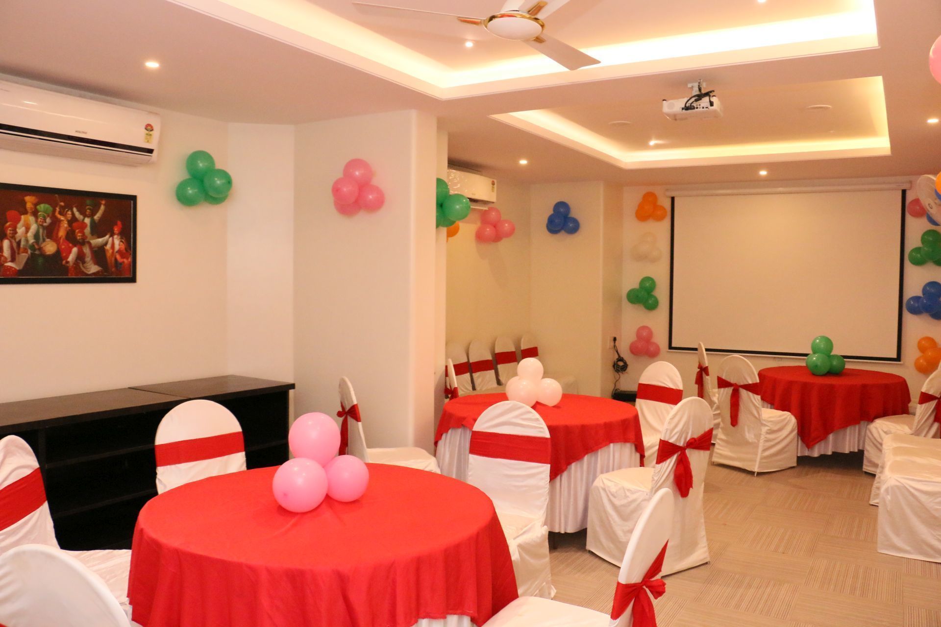 A conference room with round tables covered in red tablecloths, white chairs with red sashes, and balloons on the walls.