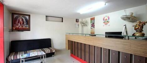 A reception area with a sofa, a glass-top desk, and a wall-mounted fan.