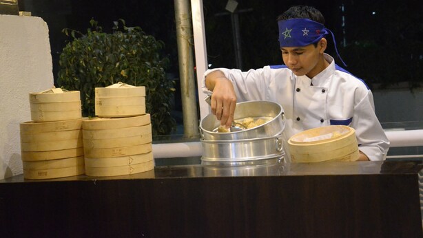 Un chef preparando comida en una barra con vaporeras de bambú apiladas y una olla.
