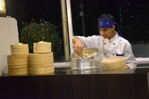 Un chef preparando comida en una barra con vaporeras de bambú apiladas y una olla.