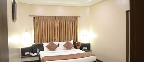 A hotel room with a bed, two bedside tables, a nightstand, a ceiling fan, and a window with curtains.