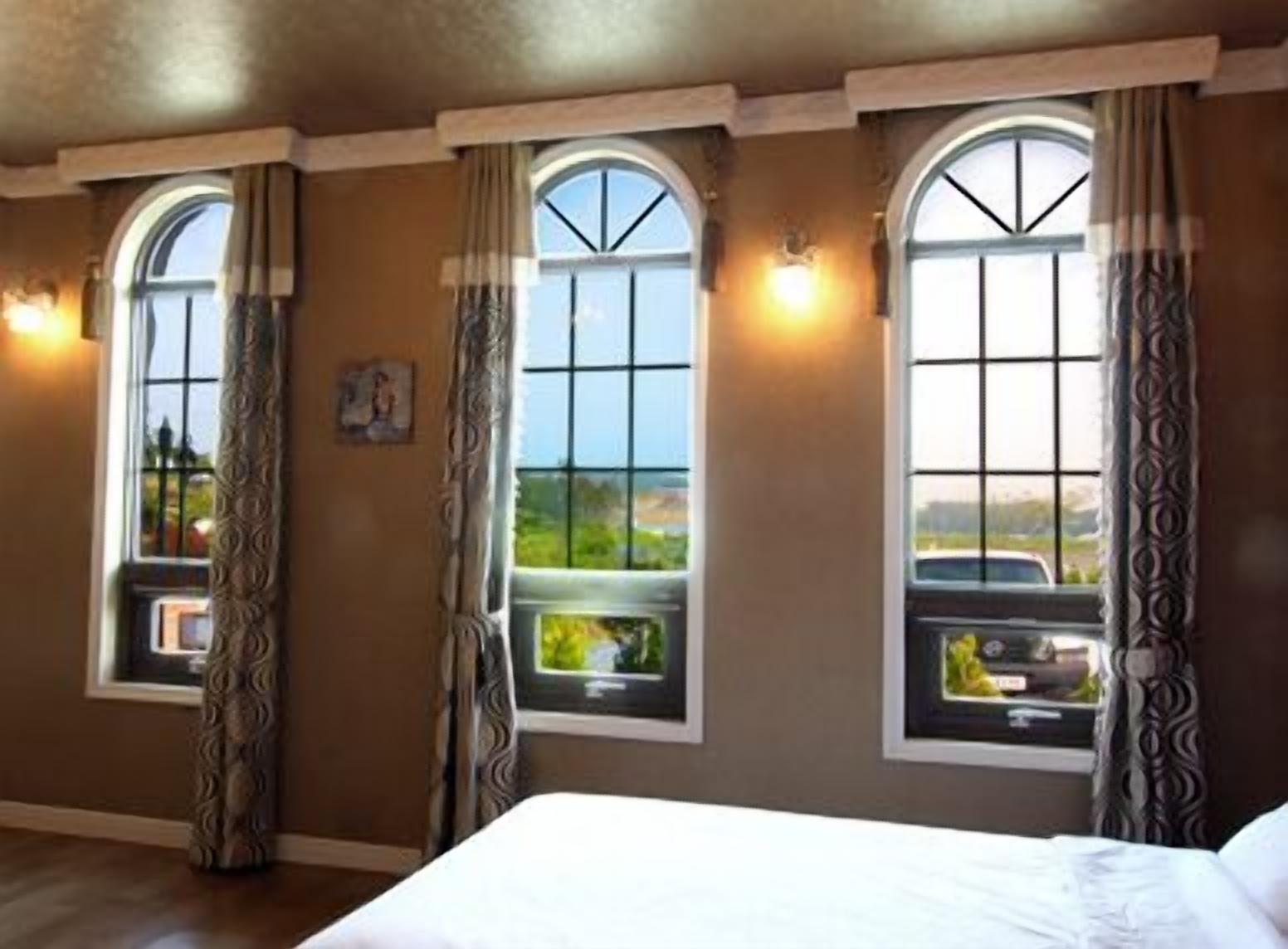 A hotel room with three arched windows, each with a view of the outdoors.