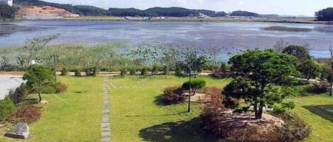 A grassy area with a stone pathway leading to a body of water, surrounded by trees and hills in the background.