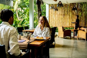 A restaurant with a wooden table, wicker chairs, and a bamboo wall.