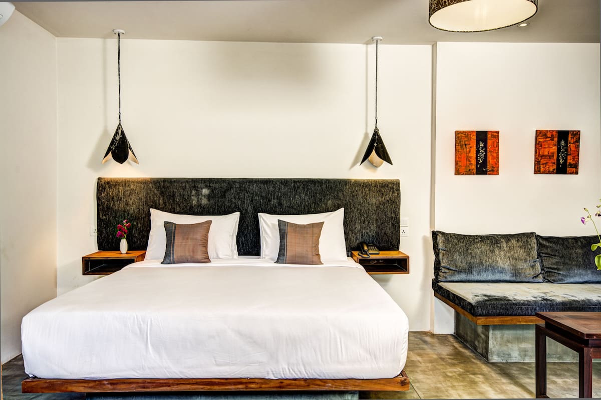 Une chambre à coucher moderne avec un grand lit, des tables de chevet, un canapé et des œuvres d’art accrochées aux murs.