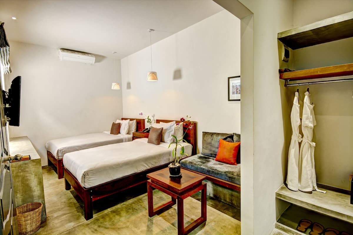 Une chambre d’hôtel avec deux lits, une petite table avec une plante, un banc et un porte-vêtements.