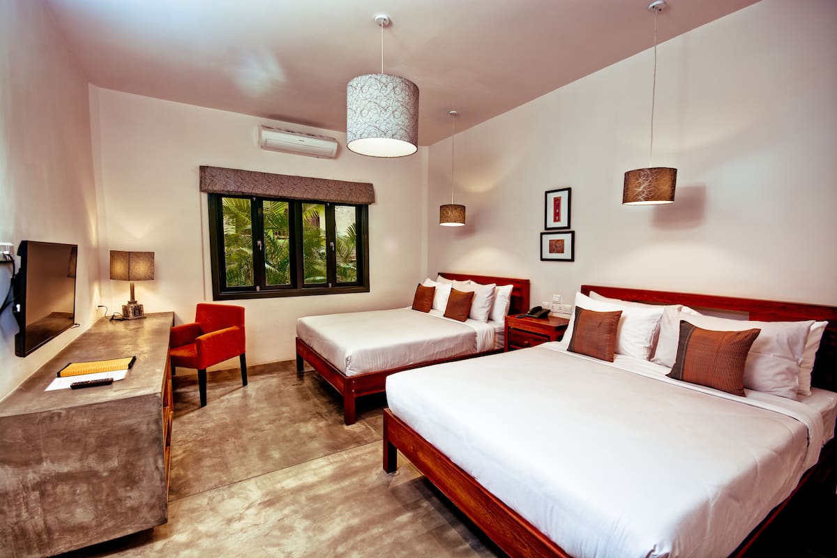 Une chambre d’hôtel avec deux lits simples, un bureau avec une chaise, une télévision et une fenêtre donnant sur un espace verdoyant.